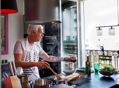 senior Italian man cooks meal drinks wine  stylish modern apartment
