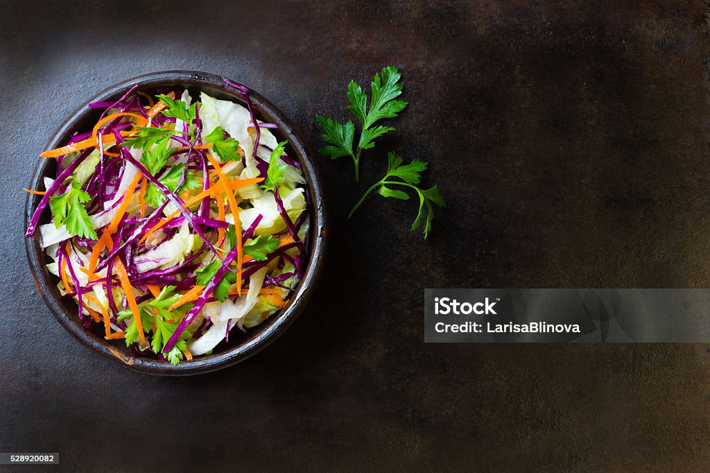 Fresh vegetables salad purple cabbage, lettuce, carrot. Top view Fresh vegetables salad with purple cabbage, white cabbage,  lettuce, carrot in dark clay bowl on black background. Top view Coleslaw Stock Photo