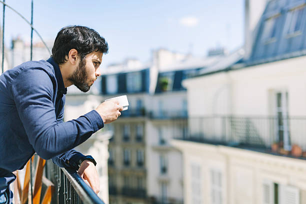 istock Young Man Drinking Coffee on a Sunny Apartment Balcony 528921870