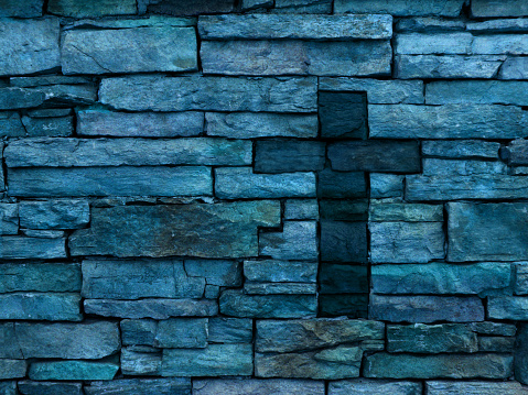 A multi colored blue rustic layered brick wall with dark inset brick Christian cross off-center. The colors on the brick wall include blue, purple, green and pink