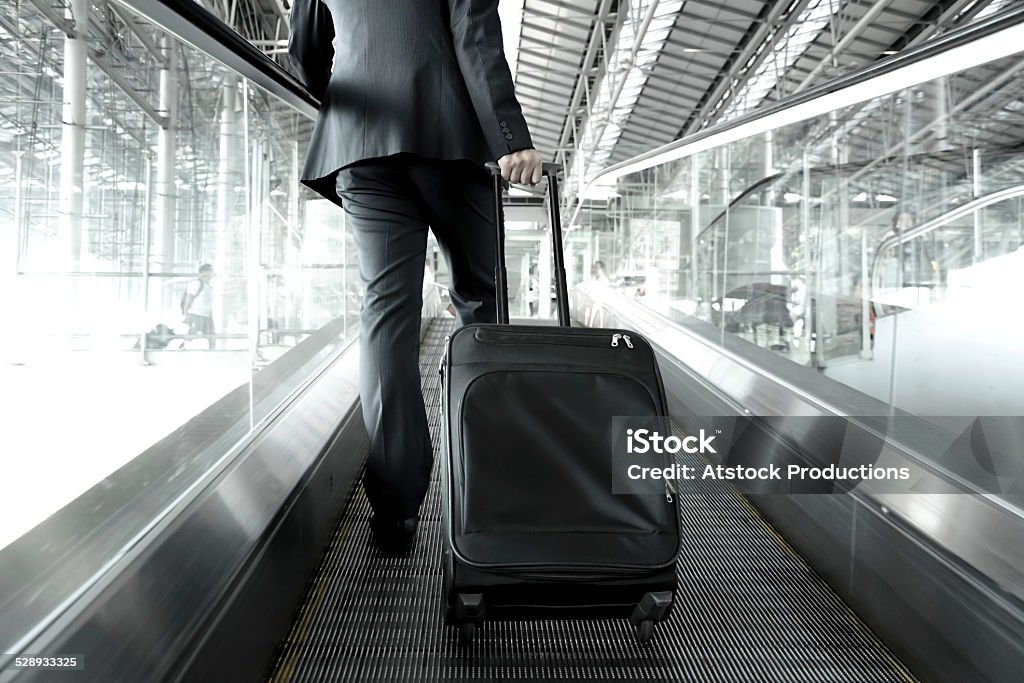 Businessman holding trolley bag going up on the escalator Businessman holding trolley bag going up on the escalator at the airport Airport Stock Photo