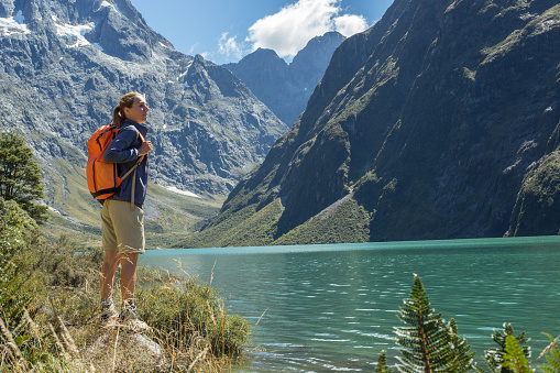 Cheerful young woman hiking reaches the lake Marian, located in the Fiordland national park, New Zealand.