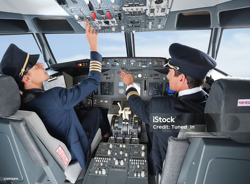 Pilot pushing button in airplane cockpit with co-pilot Pilot Stock Photo