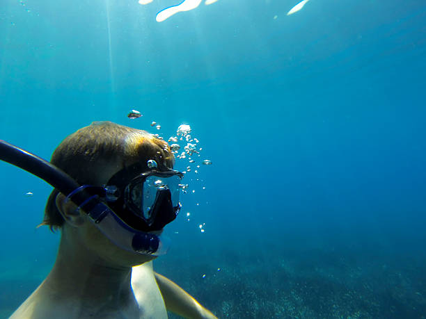Young diver blowing air under the surface in the light blue sea on sunny day.