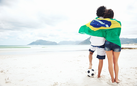 Brazil soccer fans stand on beach together with flag for world cup with ball