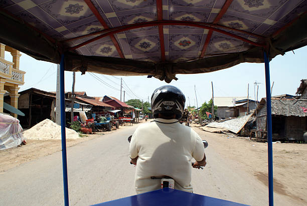 Siem Reap, Cambodia - April 27th, 2011: View from the back of a Tuk Tuk shows the passengers perspective with the back of the driver in center frame of image. 