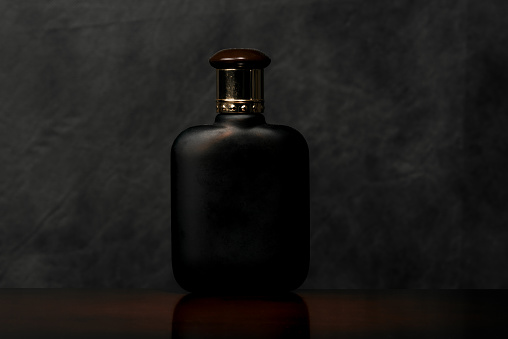 Flat scent bottle of frosted glass on a dark surface of the noble wood.