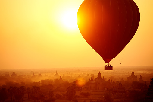 Silhouette of hot air balloon over Bagan in Myanmar, tourists watching sunrise over ancient city