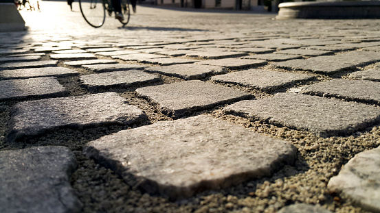Cobbled street ground, Pavement of stone cubes with bicycle and shadows of people in the background.