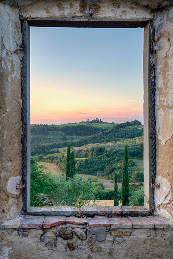 Framed view from an old window in an abandoned stone house to a green Tuscany landscape wit hills and cypresses