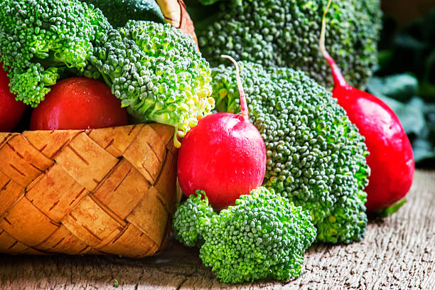 Fresh vegetables in a wicker basket: tomatoes, broccoli, cucumber, avocado, radishes, parsley, dill, vintage wooden background, selective focus