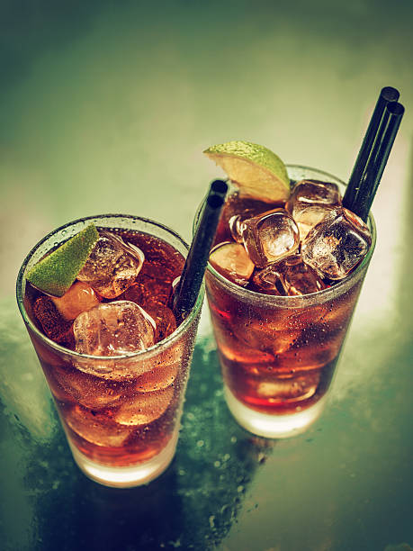 Two glasses of cold rum cola High angle view of two glasses of rum-cola cocktail with ice served on the bar. Vintage colour look. cuba libre stock pictures, royalty-free photos & images