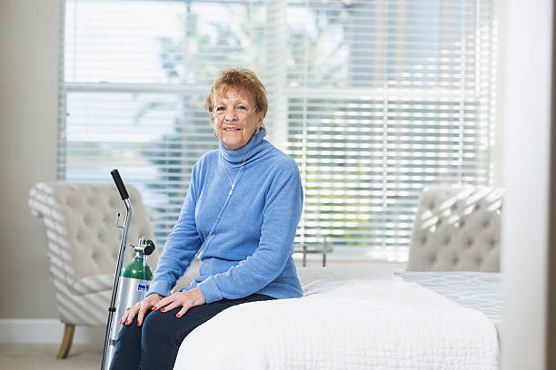 Senior woman at home with portable oxygen tank A senior woman in her 70s sitting in her bedroom with a portable oxygen tank. She is relaxed, smiling and looking at the camera. oxygen photos stock pictures, royalty-free photos & images