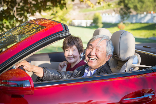 Attractive Happy Chinese Couple Enjoying An Afternoon Drive in Their Convertible.