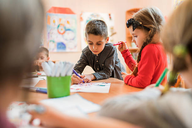 Group of small kids coloring on art class in a preschool. Focus is on little boy.