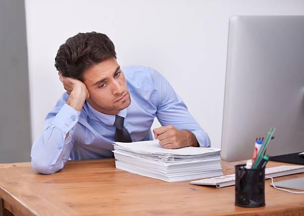 Job frustration Shot of a bored-looking office worker sitting at his computer wasting time stock pictures, royalty-free photos & images