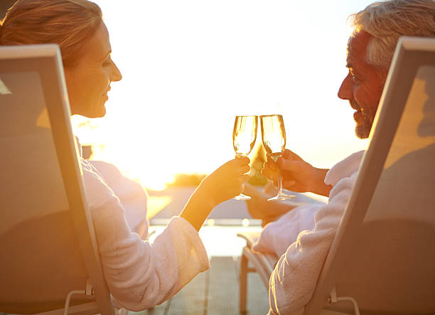 Poolside bubbly and relaxation Rearview shot of a mature couple drinking champagne while relaxing in deck chairs at sunset drinks on the deck stock pictures, royalty-free photos & images