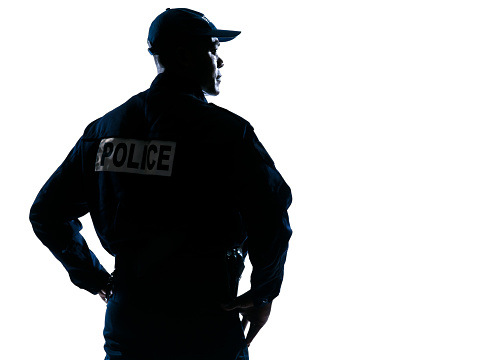 Rear view of a serious afro American policeman with hands on hip looking to his side on white isolated background