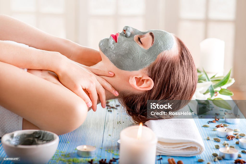 Woman with spa mask Young woman with spa facial mask on her face lying on blue table with flower, candles and sea salt in the beaty salon. Side view Adult Stock Photo