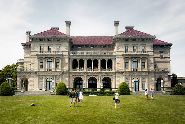 The Breakers mansion at Cliff Walk in Newport, Rhode Island Newport, United States - August 10, 2014: People are seen meandering about the lawn of The Breakers, a mansion along the historic Cliff Walk in Newport. The Breakers was built as the Newport summer home of Cornelius Vanderbilt II and was completed in 1895. editorial architecture famous place local landmark stock pictures, royalty-free photos & images