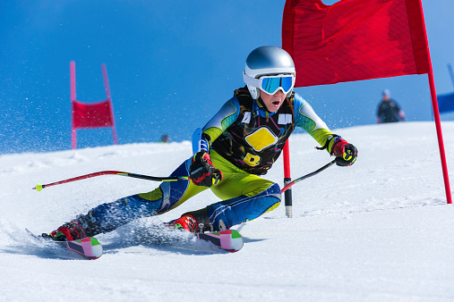 Front view of young male skier passing the red gate, giant slalom teenagers competition
