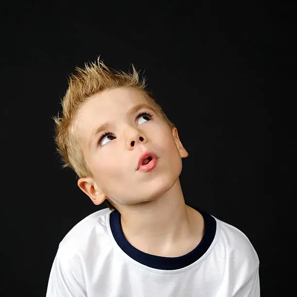 Portrait of an  young preschool boy with funny hair and face on dark background