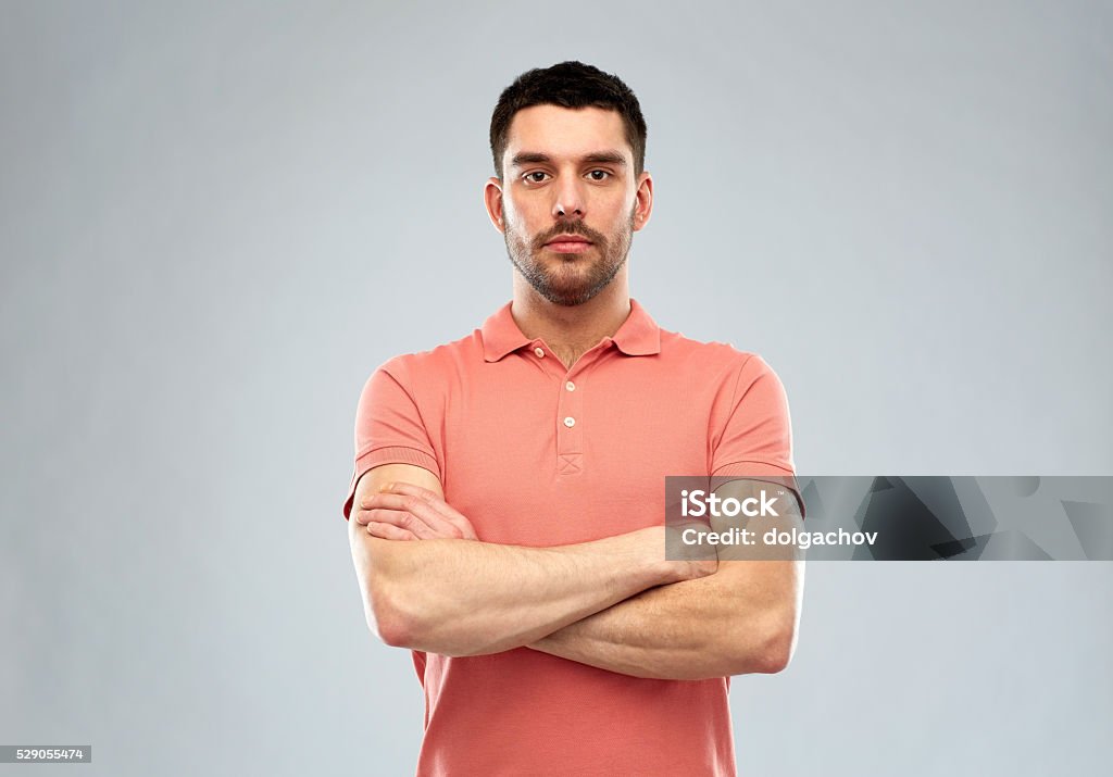 young man with crossed arms over gray background people concept - serious young man in polo t-shirt with crossed arms over gray background Men Stock Photo