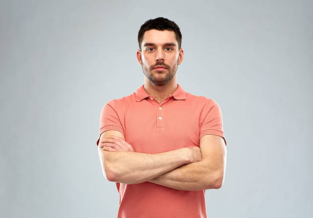 young man with crossed arms over gray background people concept - serious young man in polo t-shirt with crossed arms over gray background fine art portrait stock pictures, royalty-free photos & images