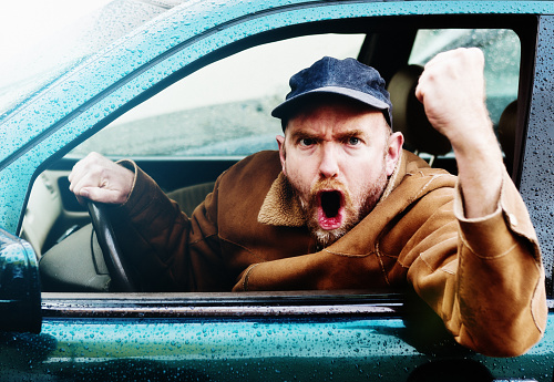 A furiously angry man driving a car yells and shakes his fist through the car window in a bout of uncontrollable road rage! He looks pretty scary!