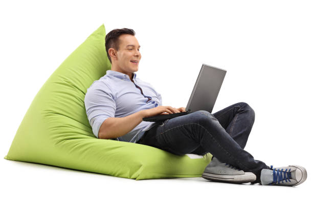 Cheerful man working on laptop Cheerful man working on laptop seated on a green beanbag isolated on white background bean bag stock pictures, royalty-free photos & images