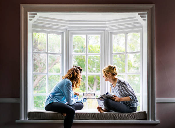Female friends using digital tablet on window sill