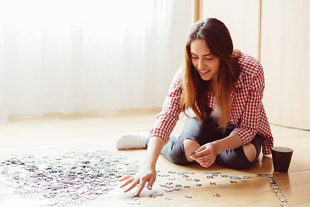Woman arranging jigsaw puzzle at home Young woman enjoying puzzle game jigsaw puzzle photos stock pictures, royalty-free photos & images