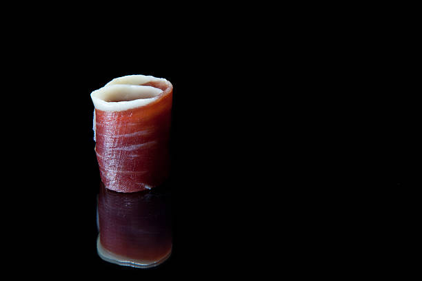 Slice of cured iberico ham isolated over black background with reflections