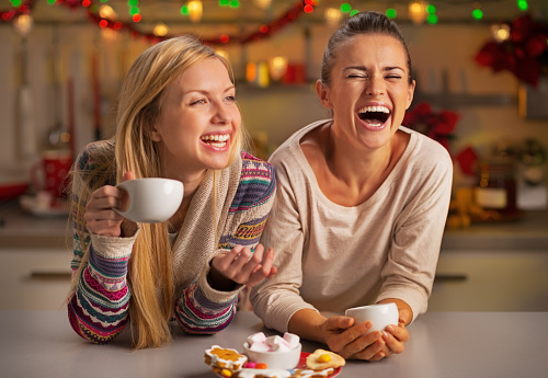 Portrait of laughing girlfriends having christmas snacks in christmas decorated kitchen