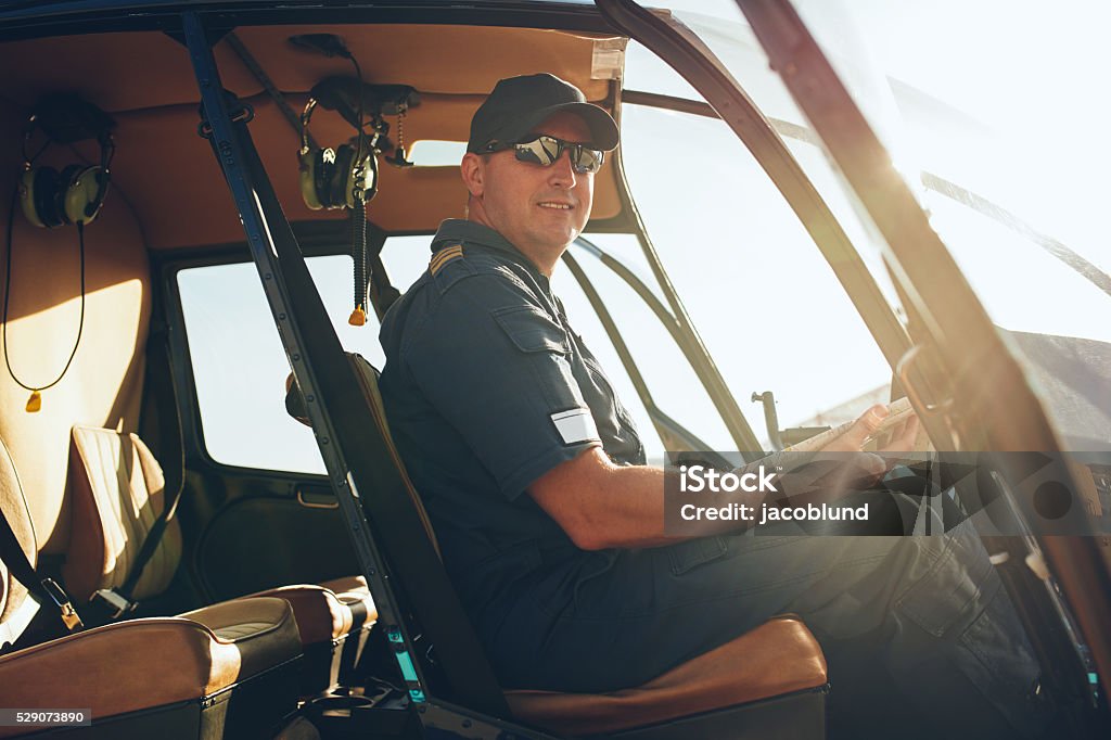 Happy male pilot in a helicopter cockpit Portrait of happy male pilot sitting in the cockpit of a helicopter with a aviation map. Helicopter Pilot Stock Photo