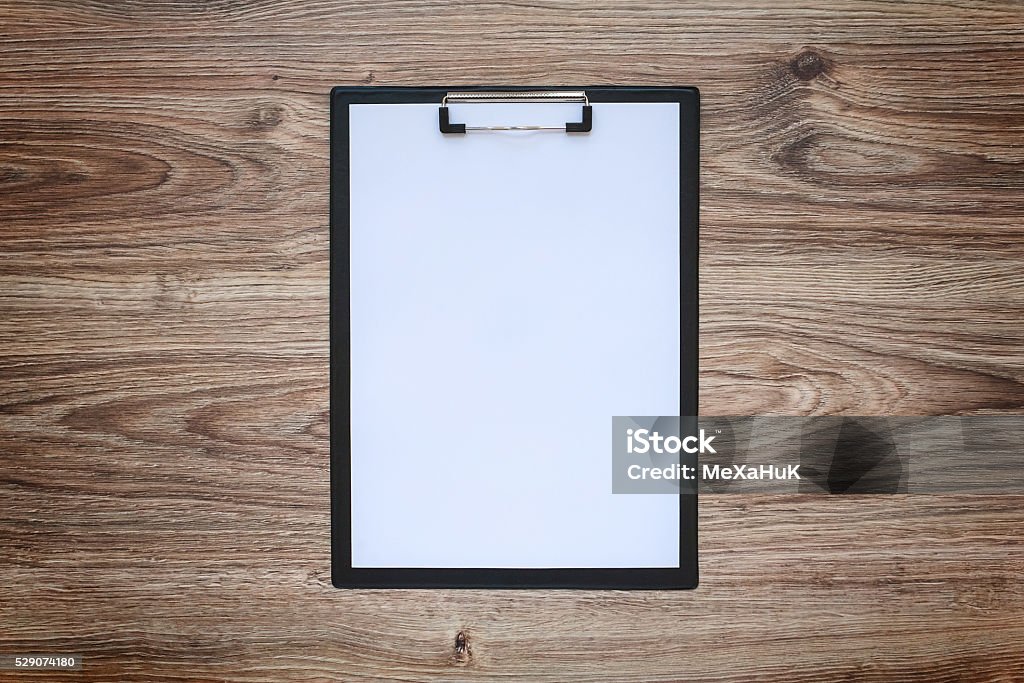 Blank white paper sheet A4 on clipboard. Wooden background. Blank white paper sheet A4 on clipboard on wooden background. Blackout frame. Top view Clipboard Stock Photo