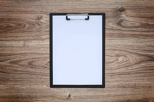 Blank white paper sheet A4 on clipboard on wooden background. Blackout frame. Top view