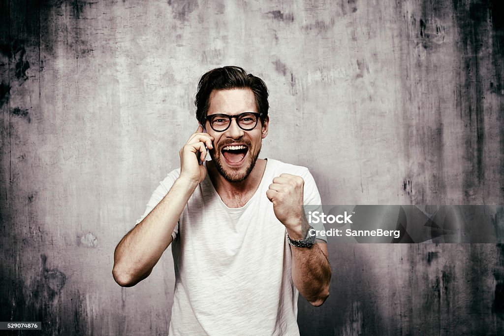 Portrait of young man celebrating on phone Punching The Air Stock Photo