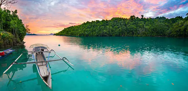 Breathtaking colorful sunset and traditional boat floating on scenic blue lagoon in the Togean (or Togian) Islands, Central Sulawesi, Indonesia, upgrowing travel destination.