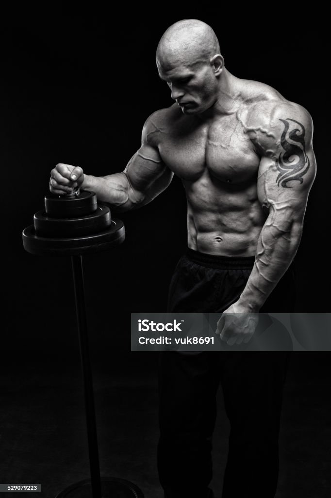 Tough guy Bodybuilder posing with barbell in front of black background 25-29 Years Stock Photo