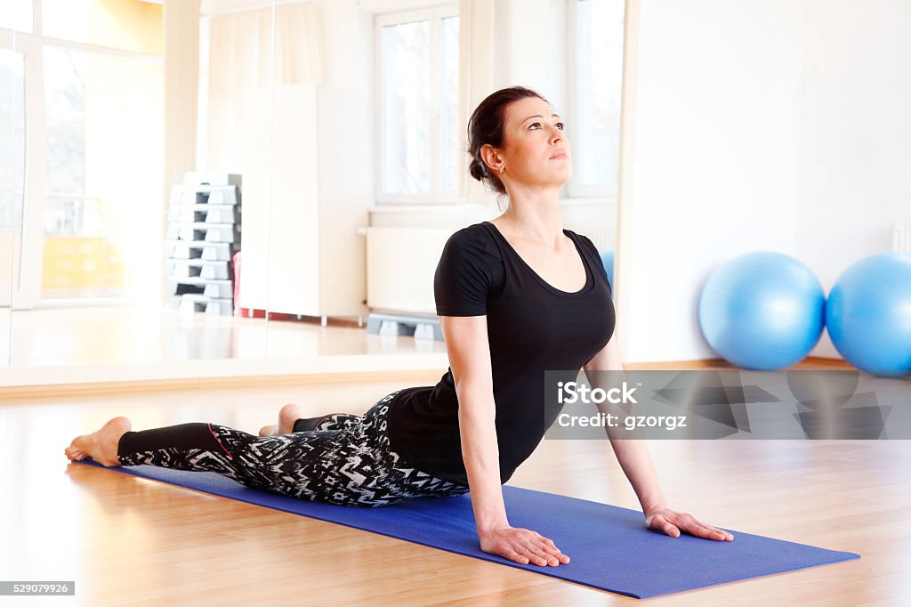 Yoga Full length portrait of a middle age woman doing cobra pose on an exercise mat at yoga studio. 30-39 Years Stock Photo