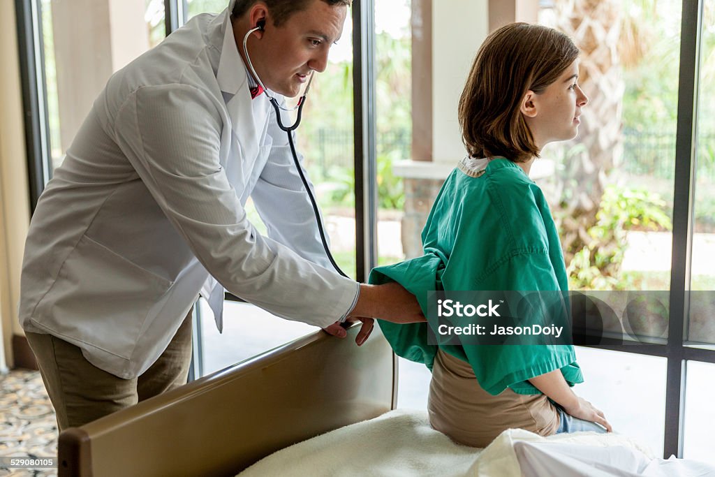 Doctor Examing Teenage Girl in Hospital A teenage patient being examined by a young doctor listening to her heart in a hospital 14-15 Years Stock Photo