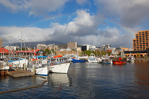 Hobart, Australia - February 10, 2013: The sun bursts through low clouds creating a faint rainbow over a fleet of fishing boats and other vessels crowding the picturesque harbour in Hobart, Tasmania.