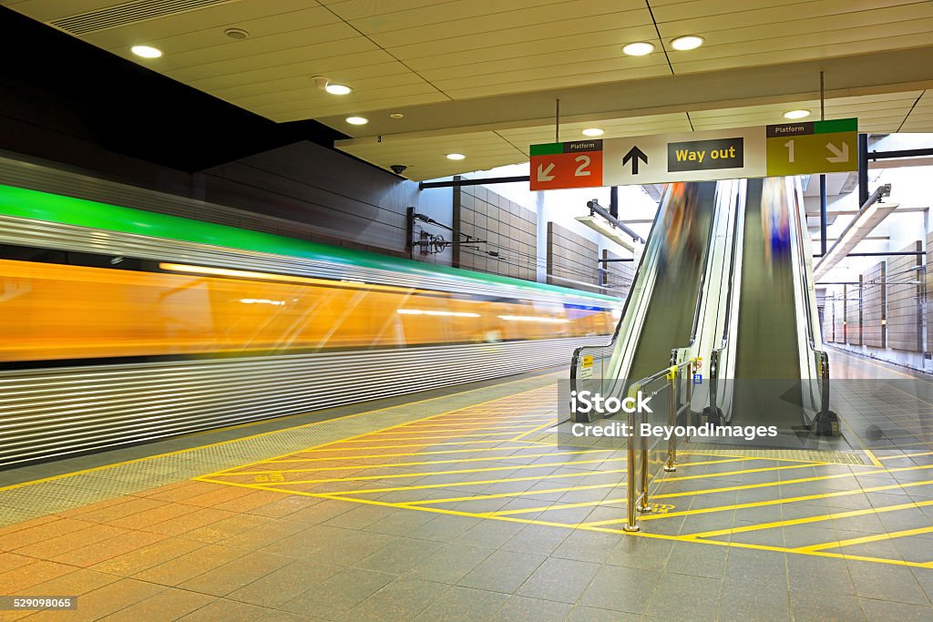 Blurred metro train departing underground station Long exposure of metro train with bright green roof departing underground station.  Escalators with blurred motion depict arriving and departing commuters.  Taken with permission of station staff & security.  Shows in-camera motion blur.  Horizontal, copy space, ID removed. Perth - Australia Stock Photo