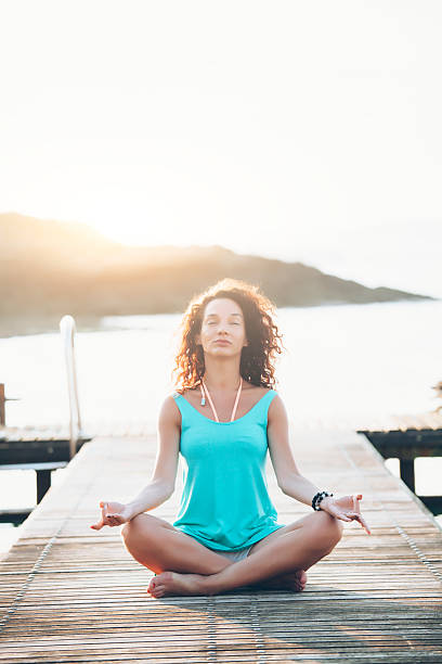 istock Young woman sitting on a pier in lotus pose 529115044