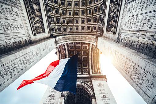 French flag below Arc de Triomphe in Paris, France. Low angle view.