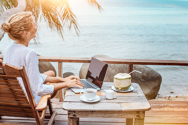 若い女性に取り組んでいるのノートパソコンで、コーヒーや若いココナッツ - on beach laptop working ストックフォトと画像