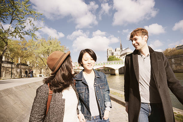 Three young friends taking a promenade in Paris, France along the River Seine, with Notre Dame cathedral in the background, on a sunny day