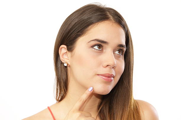 Young lady portrait with a pose looking away with a doubtful expression and one handon her chin. She is like thinking in this pose. This beautiful latin lady has light makeup and is wearing a casual shirt. She is caucassian with long smooth hair and white skin. This studio shot was taken over white background.