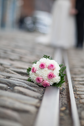 A selectively focused capture of a bouquet of pink and white flowers across railroad tracks with a blurred out bride and groom in the background.